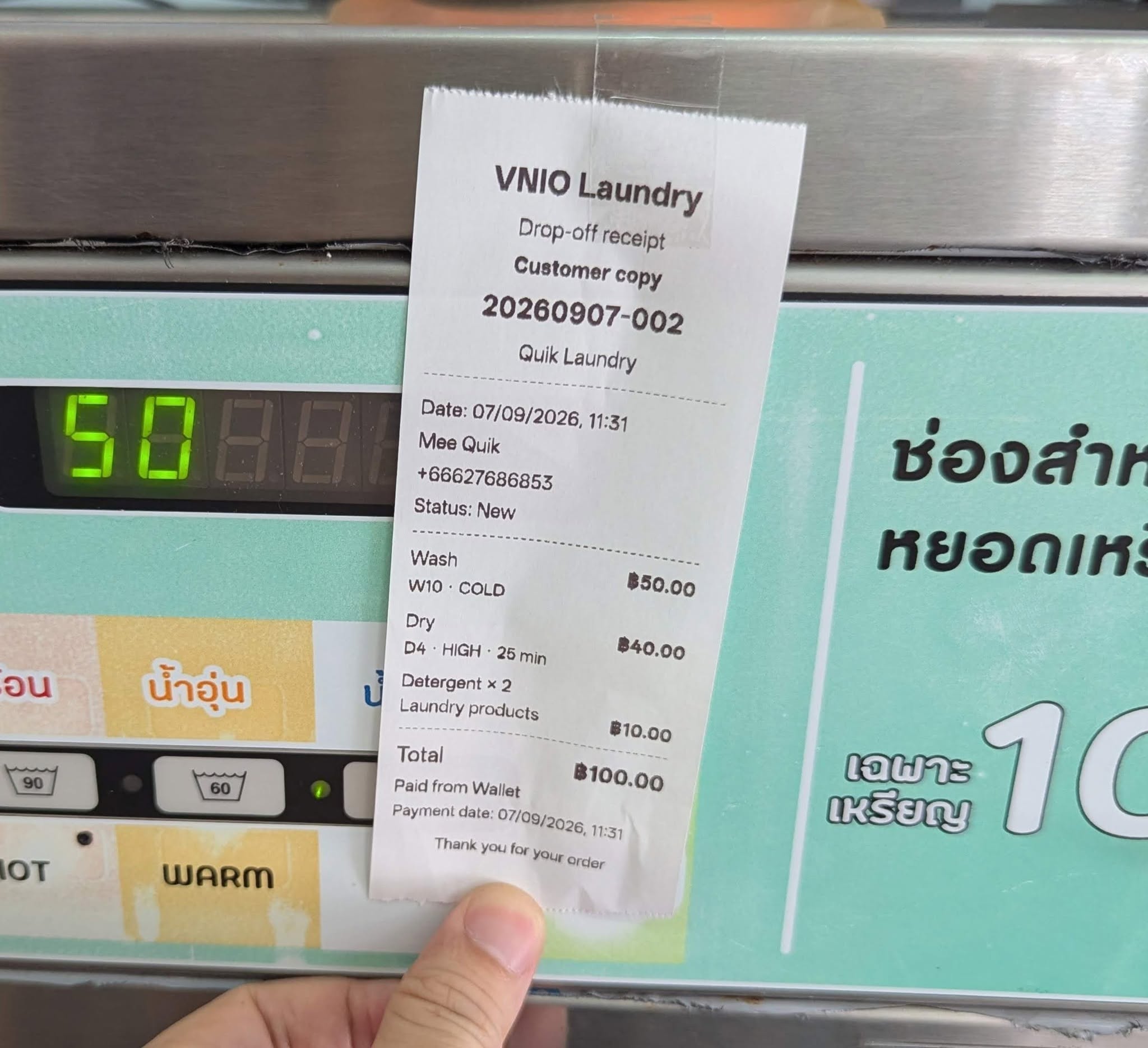 VNIO Laundry drop-off receipt held in front of a washing machine.